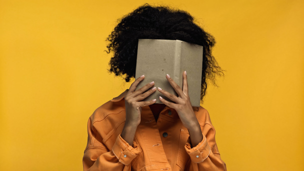 african american woman covering face with book isolated on yellow - Foto, immagini