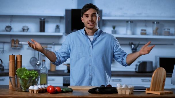 young man looking at camera while gesturing near table with fresh ingredients - Photo, Image
