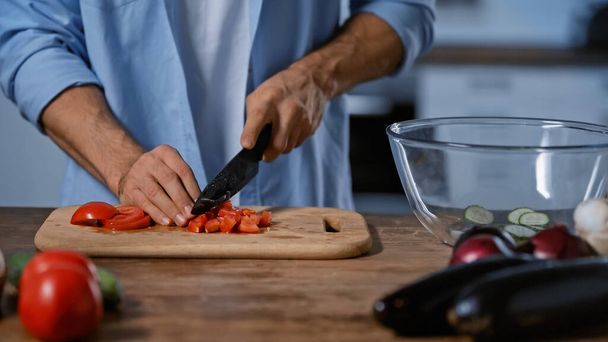 cropped view of man cutting tomatoes near blurred eggplants and glass bowl - Foto, Imagen