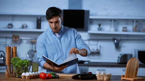 young man reading recipe book near table with fresh ingredients - Foto, Imagem