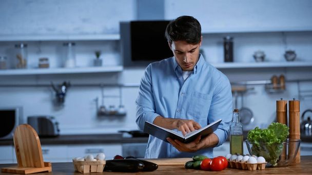 young man reading recipe book near table with fresh vegetables - Foto, imagen