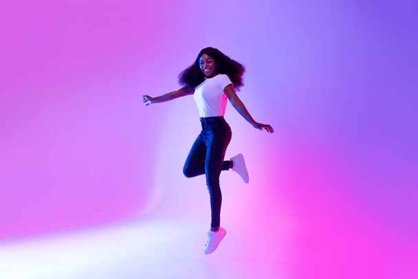Полнометражный портрет активной энергичной афроамериканской женщины тысячелетия, прыгающей в неоновом свете, копирующее пространство - Фото, изображение