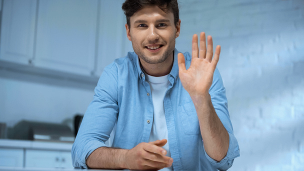 happy man looking at camera and waving hand in kitchen - 写真・画像