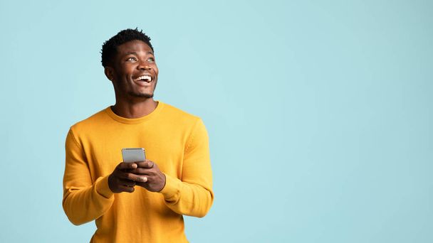 Homme noir joyeux utilisant un smartphone, regardant l'espace de copie - Photo, image