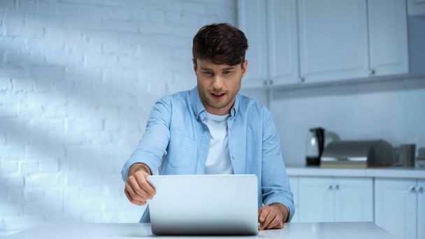 man in blue shirt looking at laptop while working in kitchen - Foto, Bild