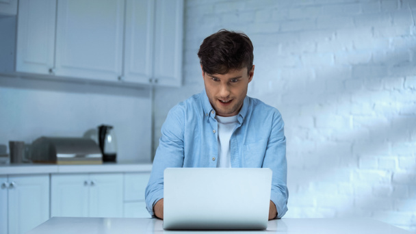 astonished freelancer in blue shirt working on laptop in kitchen - 写真・画像