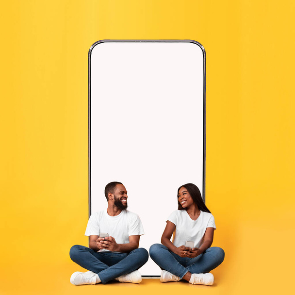 Black couple sitting near blank empty smartphone screen for mockup - Foto, imagen