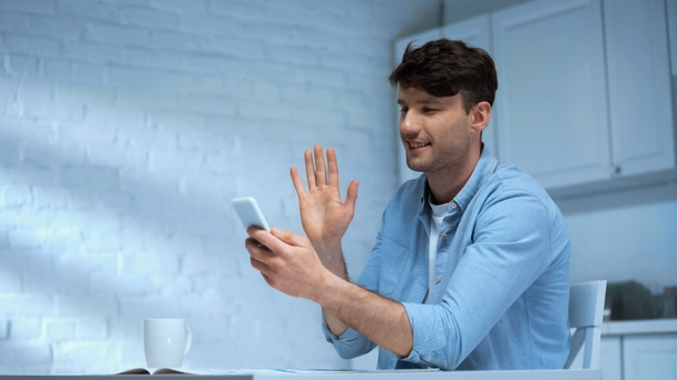happy man waving hand during video call on smartphone in kitchen - Photo, Image
