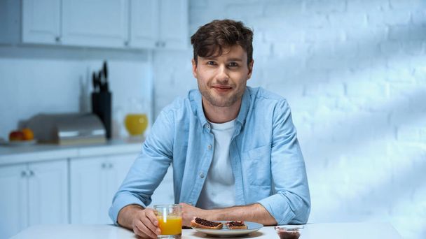 boldog ember nézi a kamerát, miközben ül közel finom reggeli a konyhában - Fotó, kép