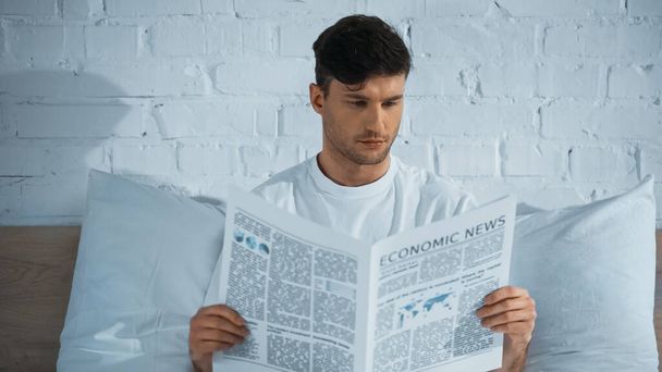 man reading economic news while sitting in bed in morning - Photo, image