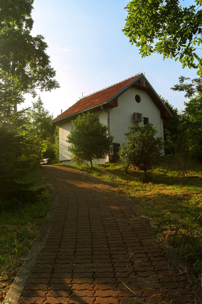 Egy kis gyönyörű ház a hegyek lábánál, napfénnyel borítva és egy zöld kert, burgundia járdával. - Fotó, kép
