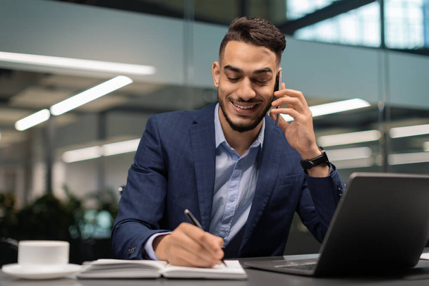 Успешный ближневосточный предприниматель, работающий в офисе, разговаривающий по телефону - Фото, изображение