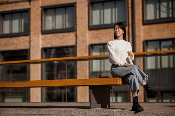 Girl sitting waiting on bench on background of building - Foto, imagen