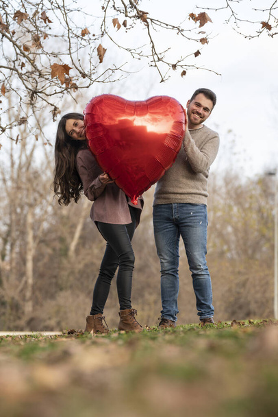Молодая пара празднует День Святого Валентина с воздушным шаром в форме сердца - Фото, изображение