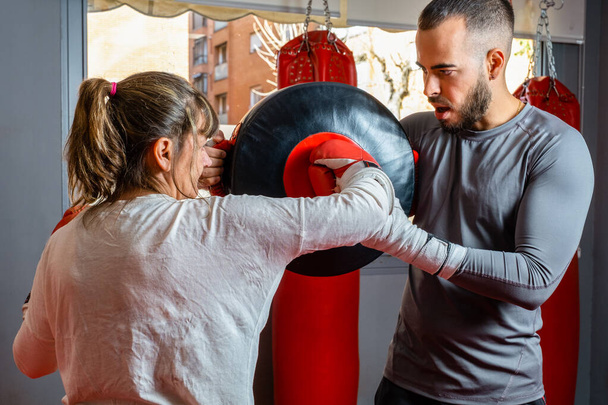 volwassen vrouw gooien punch naar haar boksleraar training handschoen - Foto, afbeelding