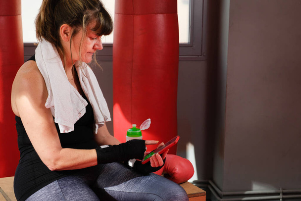 Reife Frau ruht sich beim Training in der Boxsporthalle aus - Foto, Bild