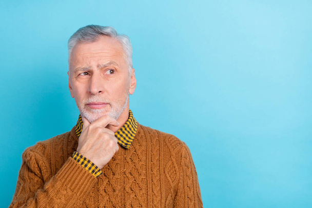 Photo of doubtful unsure man pensioner dressed brown pullover arm chin looking empty space isolated blue color background - Фото, изображение