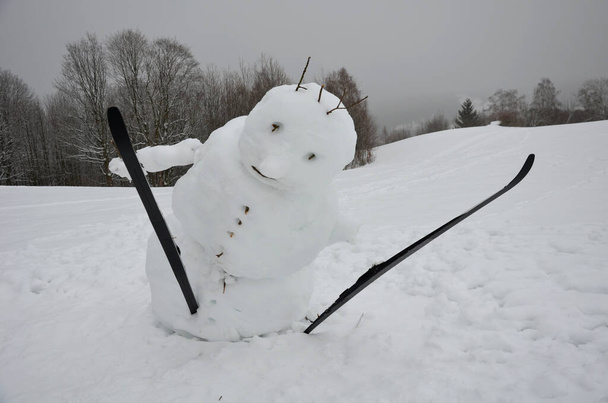 Il grande pupazzo di neve ha un corpo inclinato che sembra stia cadendo. ha bastoni da sci e sci di fondo. mascotte che salta. lenta fusione econgelamento inclina il baricentro - Foto, immagini