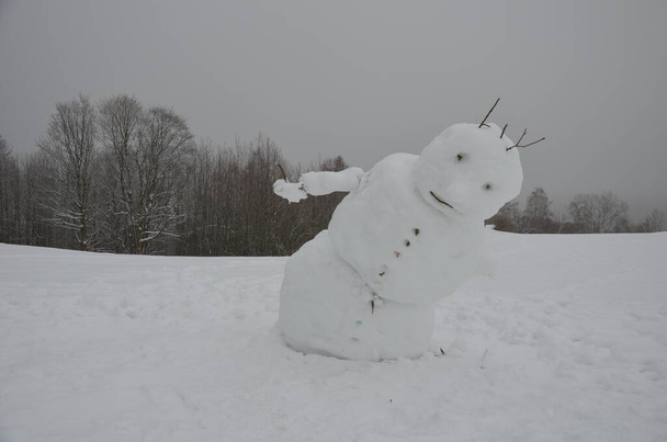 ένας μεγάλος χιονάνθρωπος έχει ένα επικλινές σώμα που μοιάζει σαν να πέφτει, δεν κουτσαίνει, και έχει πόνο στην πλάτη. Φεύγοντας ο χειμώνας τελείωσε. προς τα εμπρός στροφή - Φωτογραφία, εικόνα
