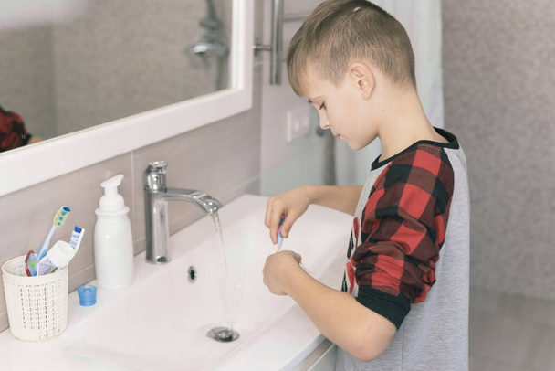 Un ragazzino biondo che impara a lavarsi i denti in bagno. Il ragazzo sta imparando a stare in salute. Concetto sanitario
. - Foto, immagini