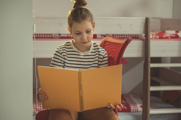 Teen blonde girl reading text in notebook at home - Valokuva, kuva