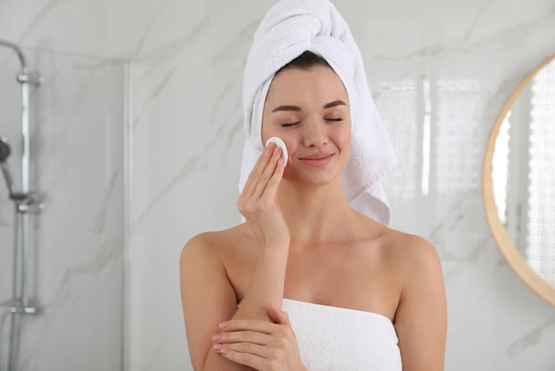 Beautiful young woman with hair wrapped in towel cleaning her face indoors - Foto, Imagem