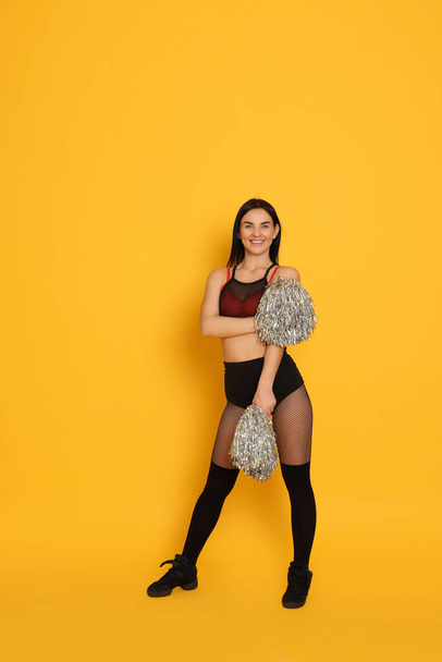 Beautiful cheerleader in costume holding pom poms on yellow background - Photo, Image