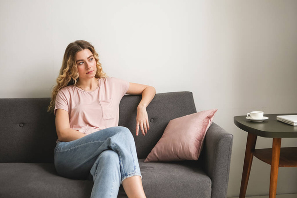 Beautiful young woman sitting on gray sofa in the room. Resting girl in pink shirt. Relaxing woman - Foto, Imagen
