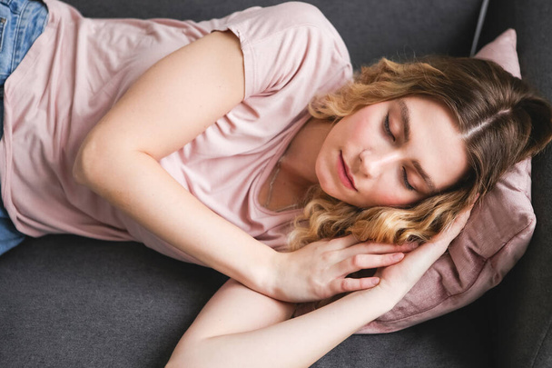 Beautiful young woman sleeping on gray sofa. Girl in pink shirt resting at home after work. - Fotoğraf, Görsel