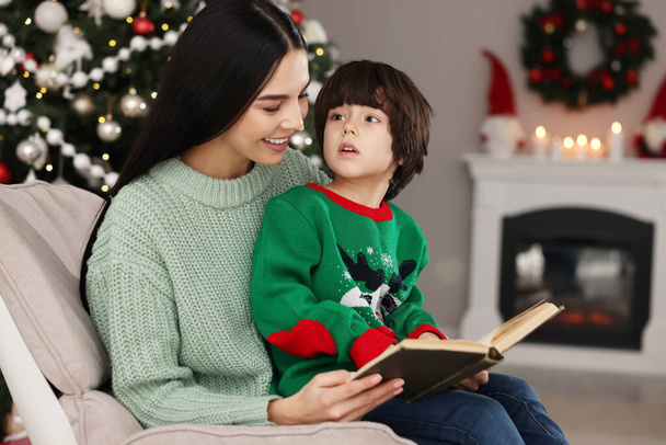 Mother with her cute son reading book in room decorated for Christmas - Foto, afbeelding
