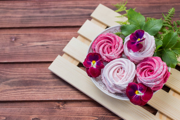 Gyönyörű finom desszert. Rózsaszín zephyr fa háttér és rózsaszín virágok.Plate bogyó, Meringue zephyr desszert. - Fotó, kép