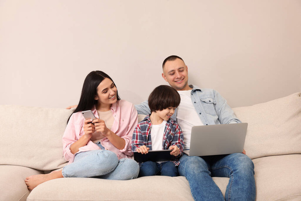 Happy family with gadgets on sofa at home - Φωτογραφία, εικόνα