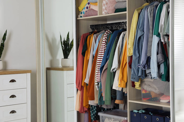 Wardrobe closet with different stylish clothes and home stuff in room. Fast fashion - Zdjęcie, obraz