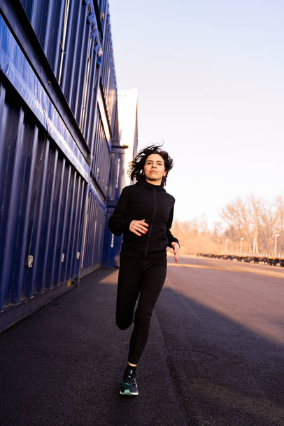 young adult woman is running in the morning among the shipping containers of a commercial port - Concept of sport and wellness - Valokuva, kuva