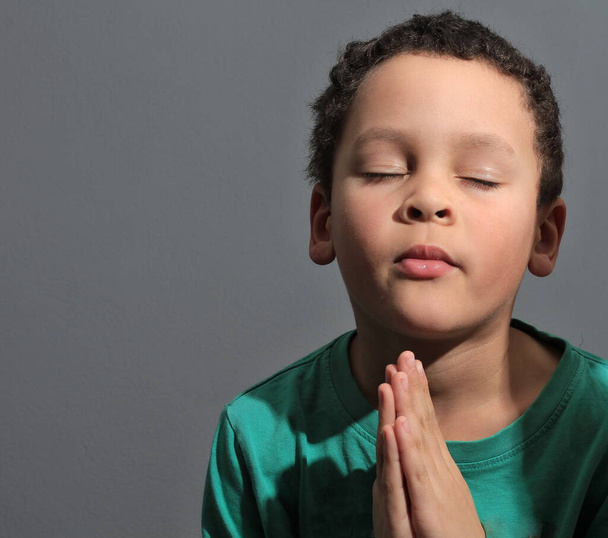 chłopiec modląc się do Boga z rękami trzymanymi razem z zamkniętymi oczami z ludźmi Zdjęcie Zdjęcie - Zdjęcie, obraz