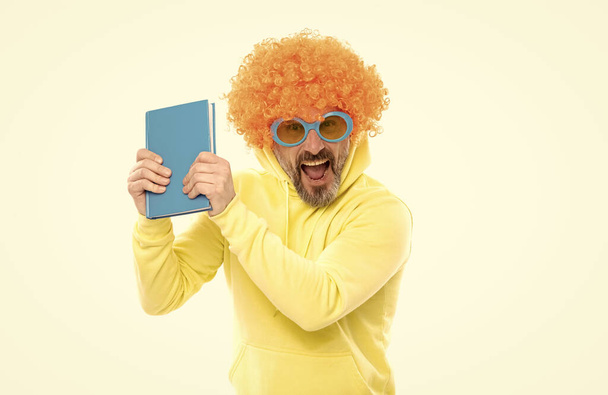 Crazy δάσκαλος σε πορτοκαλί περούκα με funky γυαλιά ηλίου φωνάζουν δυνατά κρατώντας βιβλίο βιβλιοθήκης, σχολείο - Φωτογραφία, εικόνα