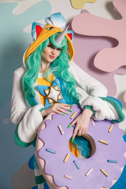 A girl dressed as a unicorn with a huge donut in her hands. - Φωτογραφία, εικόνα