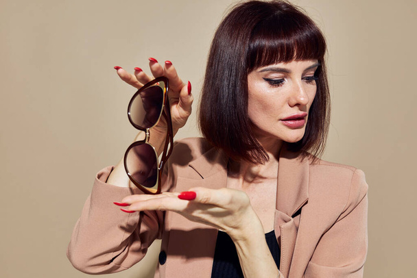 beautiful woman in sunglasses short haired suit gesturing with hands light background - Φωτογραφία, εικόνα