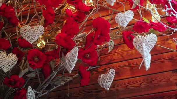 聖バレンタインデーのスクリーンセーバー。木のスイングからぶら下がる白いハート型の装飾と光と花で乾いた枝を照らす背景に吹き付けるスピン - 映像、動画
