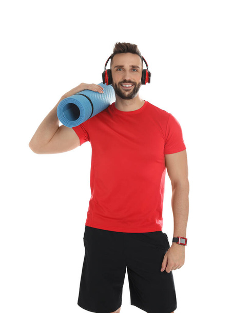 Handsome man with yoga mat and headphones on white background - Photo, image