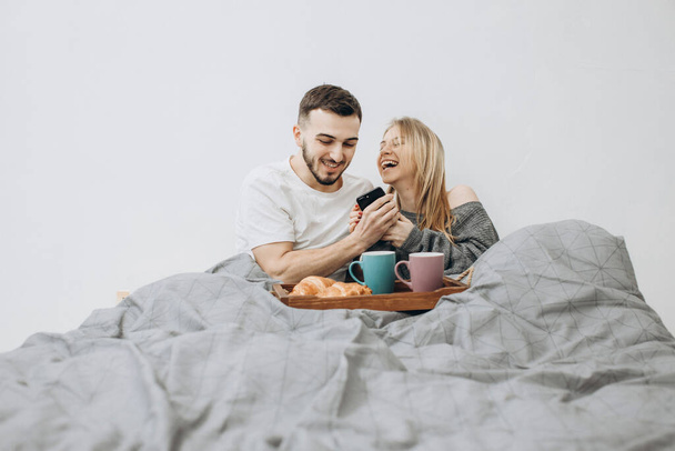 ロマンチックな幸せなカップルがベッドで朝食を持っている - 写真・画像