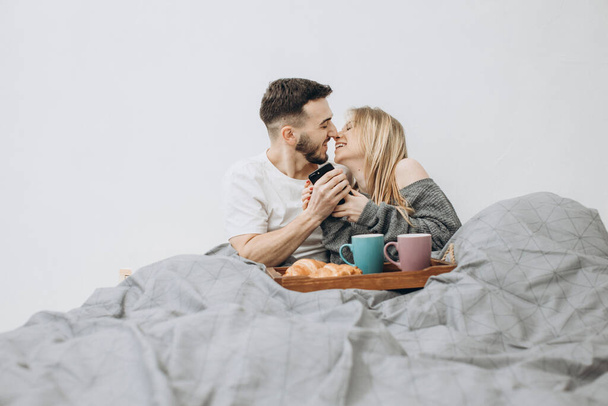 ロマンチックな幸せなカップルがベッドで朝食を持っている - 写真・画像