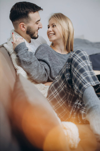 Couple in love sitting on the couch in the living room, wearing pajamas after getting up in the morning, enjoying the morning and having breakfast - Фото, изображение