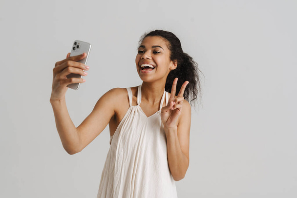 Black young woman gesturing while taking selfie on cellphone isolated over white background - Valokuva, kuva