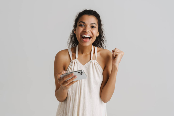 Black young woman playing online game on mobile phone isolated over white background - Φωτογραφία, εικόνα