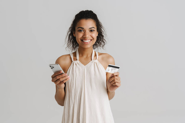 Черная молодая женщина позирует с мобильного телефона и кредитной карты изолированы на белом фоне - Фото, изображение