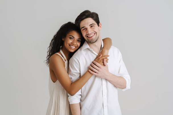 Young multiracial couple hugging and smiling at camera isolated over white background - Foto, imagen