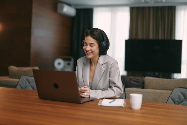 Happy young girl businesswoman in headphones watching webinar on laptop, conduct video call with clients or partners - Fotó, kép