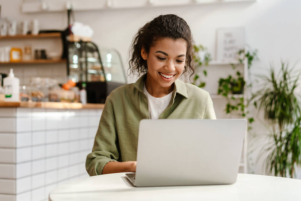 Young black woman working with laptop while sitting in cafe indoors - Foto, Bild