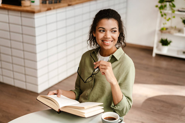 Kafede kahve içerken kitap okuyan genç siyah bir kadın. - Fotoğraf, Görsel